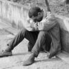 man in gray jacket and black pants sitting on concrete bench