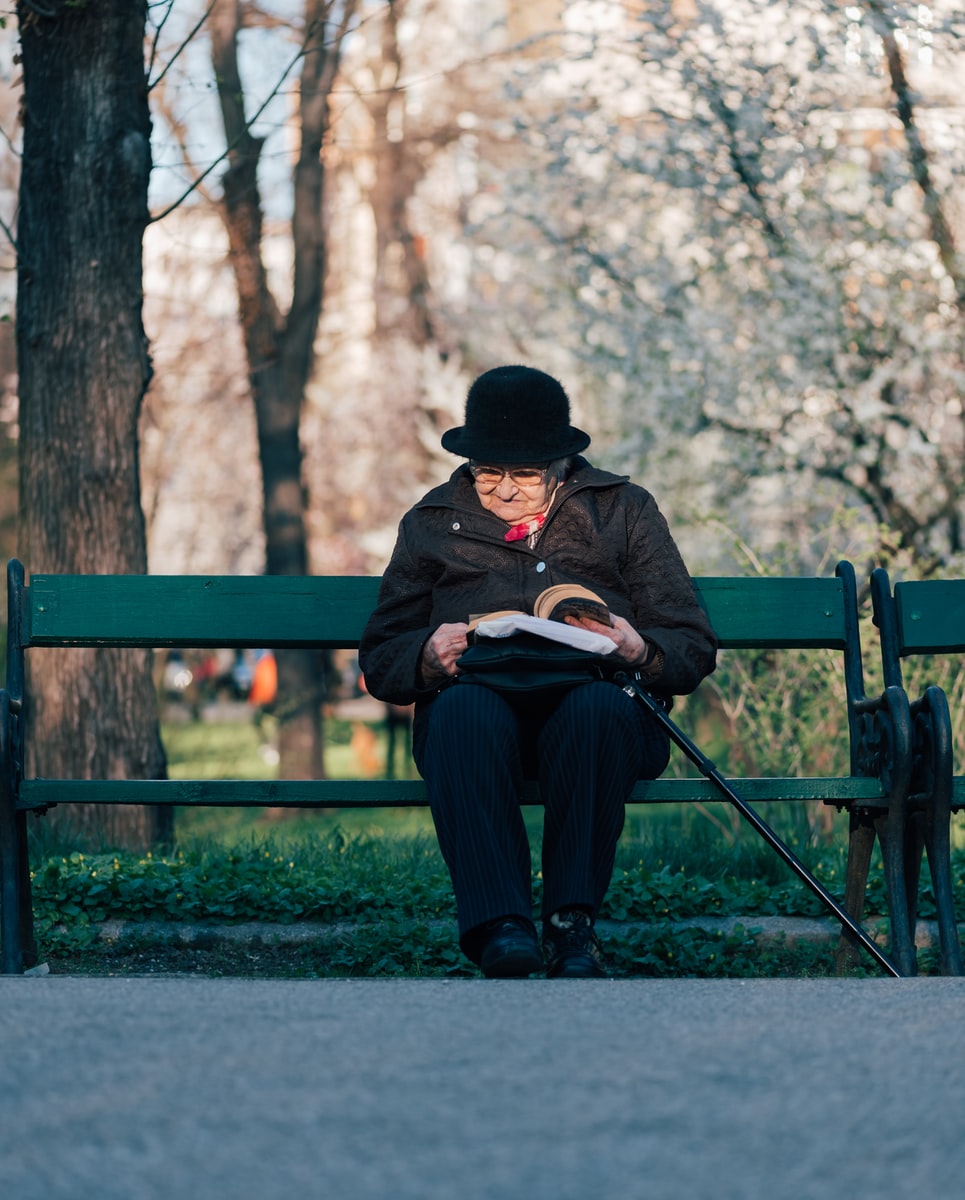 person sits on bench reading book in front of tree at daytime