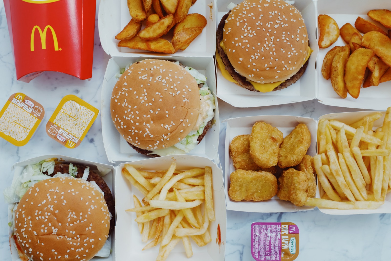 Top view flat lay of junk food including burgers with french fries and nuggets placed on marble table